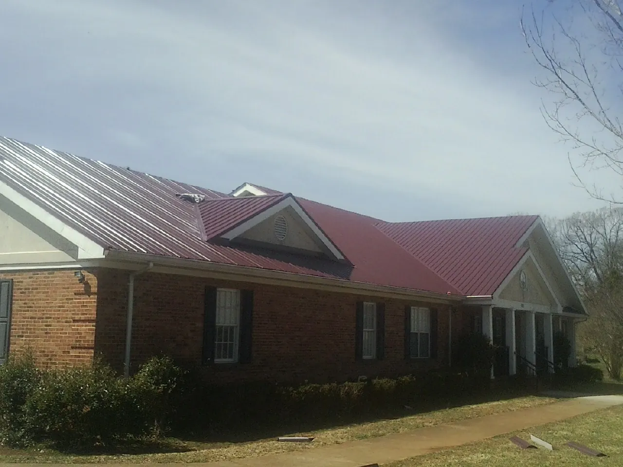 Red metal roof with gabled entries on a long brick building, from a Hail Damage Roof Repair job in Andover
